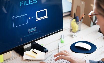 Person mit Brille sitzt vor Laptop, auf dessen Display sind Files, die hochgeladen werden mit Schaltfläche Start